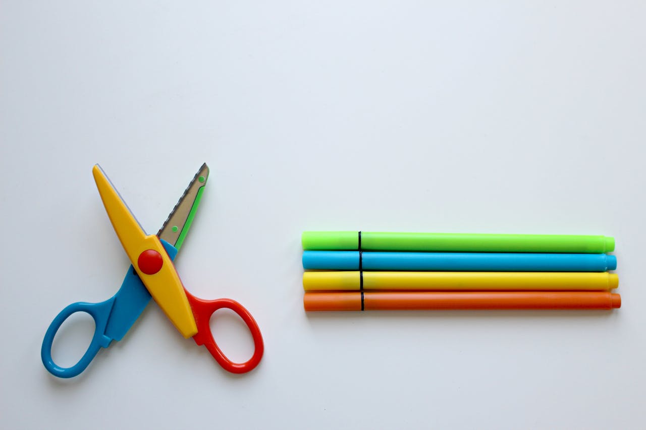 Bright stationery set on a white background with colorful scissors and markers.